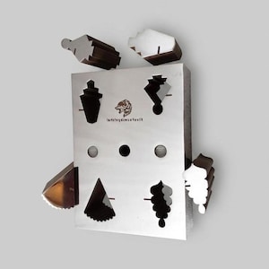 Puede incluir: Una placa rectangular de metal plateado con varios recortes y formas geométricas, incluyendo un logotipo central de cabeza de lobo con texto. Varias piezas metálicas separadas con perfiles coincidentes están colocadas alrededor de la placa principal, que tiene una superficie lisa y reflectante y múltiples orificios circulares.