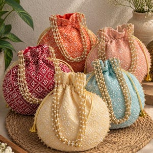 May include: A collection of five round drawstring pouches in orange, red, peach, light blue, and yellow. Each pouch features a white geometric embroidered pattern and a long, multi-strand handle made of small white faux pearls with gold accents.
