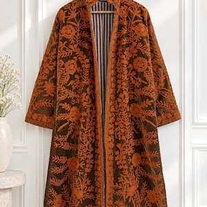 May include: A long, open-front coat in dark brown velvet featuring intricate, dense orange floral and vine embroidery across the entire surface. The garment has a high collar, long sleeves, and a vertical striped lining visible at the front opening.