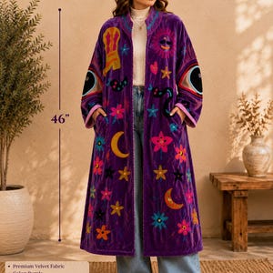 Pode incluir: Um quimono longo tipo duster em veludo roxo com bordados multicoloridos de botas, sóis, luas, estrelas, flores e olhos. A peça é aberta na frente, mede 116,84 cm de comprimento e possui mangas compridas com punhos listrados.