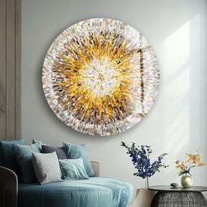 May include: A circular artwork with a mosaic design in gold, silver, and white tones. The art piece hangs on a wall above a teal circular sofa with cushions. The room has a modern design, with a round coffee table and flowers.