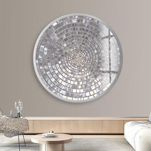 May include: A large, circular wall mirror featuring a silver mosaic tile design arranged in a spiral. The mirror has a white frame and is mounted on a neutral wall. The mirror's diameter is approximately 122 cm.