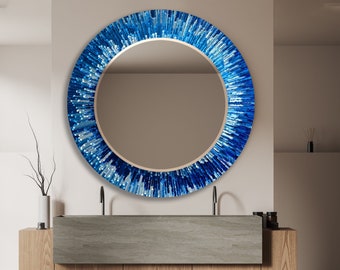 May include: A round mirror with a blue and white mosaic design. The mirror is hanging on a white wall above a wooden vanity with a gray countertop.