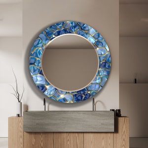 May include: A round mirror with a blue and gold mosaic design. The mirror is hanging on a white wall above a wooden vanity with a grey countertop.