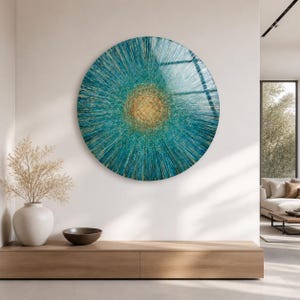 May include: A large circular wall art piece featuring a radial pattern of teal and blue lines extending from a central golden core. The artwork displays a textured, sunburst-like design with deep blue tones transitioning into lighter teal and gold.