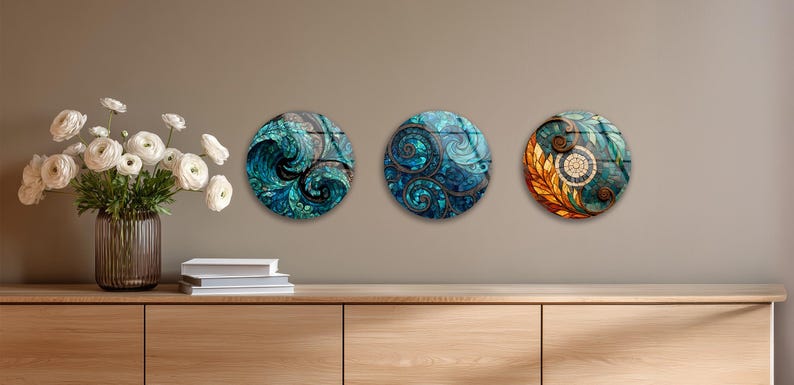 a wooden cabinet with three round wall art pieces hanging above it. On the left side of the cabinet, there is a vase filled with white flowers, and on the right side, there are two books.