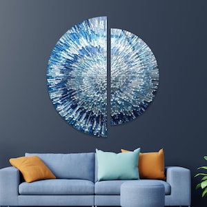 May include: Two blue and white abstract wall art pieces in the shape of half circles. The pieces are made of a textured material and have a 3D effect. The pieces are hanging on a dark blue wall above a blue sofa with orange and blue cushions.