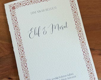 May include: A white wedding certificate with a decorative border of pink and gold floral designs. The text "DINI NIKAH BELGESI" is at the top of the certificate, followed by the names "Elif & Mesut". The bottom of the certificate includes a quote in Turkish: "Allah sevdigi kulunun kalbini sevdigi kulunun kalbiyle birleştirit Hz. Muhammed sav"