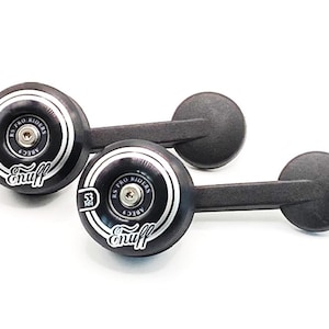 May include: Two black skateboard wheels with integrated black mounting arms. Each wheel features white circular graphics, the text Enuff, the number 53 mm, and the label RS PRO RIDERS ABEC 9. The wheels have a central silver-coloured metal bolt.