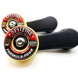 May include: Two yellow skateboard wheels with black and red graphics. The wheels have the text "Spitfire Formula Four" printed on them. The wheels are attached to black plastic handles.