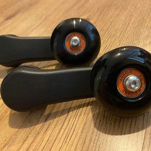 May include: Two black skateboard wheels with orange lettering. The wheels have a black plastic handle attached to them. The lettering on the wheels says "ABEC-9 RS PRO RIDERS".