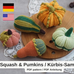 Puede incluir: Un conjunto de cuatro calabazas y calabacines de ganchillo en varios colores, incluyendo verde, naranja, rosa y marrón. Las verduras de ganchillo se muestran sobre una superficie de madera con un mantel de encaje blanco.