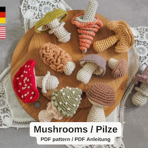 May include: A collection of various crochet mushrooms in different colors and styles, including red, green, and brown. The mushrooms are arranged on a wooden surface. The image includes the text "Mushrooms / Pilze".
