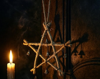 Puede incluir: Una estrella rústica de cinco puntas hecha de cuerda, adornada con pequeñas campanas, cuelga de una manija de puerta negra. Una vela encendida en un candelabro de latón proyecta un brillo cálido, creando un ambiente místico. La sombra de la estrella es visible en la puerta texturizada.