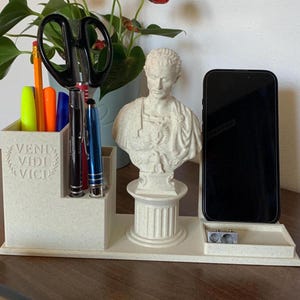 Może przedstawiać: Biały organizer na biurko z popiersiem rzymskiego cesarza, uchwytem na telefon i stojakiem na ołówki. Stojak na ołówki ma etykietę z napisem "Veni Vidi Vici".