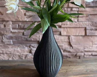 May include: A black vase with a ribbed design holds a bouquet of white peonies. The vase is sitting on a wooden surface.