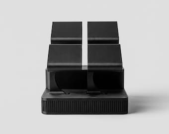 May include: A black desk organiser with four sections. The organiser has a rectangular base with vertical lines and a minimalist design. The sections are elevated and separated by a white line.