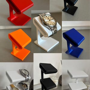 Puede incluir: Variaciones de un soporte para reloj en diferentes colores, incluyendo rojo, naranja, blanco, negro y azul. El soporte est&aacute; dise&ntilde;ado para sostener un reloj de lado. El soporte est&aacute; hecho de un material impreso en 3D. La imagen tambi&eacute;n muestra un soporte para reloj de dos niveles en blanco y negro.