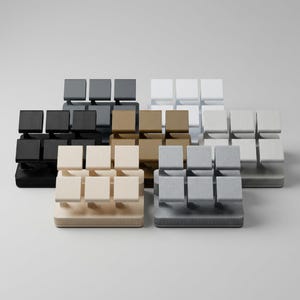 Puede incluir: Una colección de modernos y minimalistas expositores en varios colores neutros, incluyendo negro, blanco, gris y beige. Cada expositor presenta una base rectangular y múltiples plataformas cuadradas, ideales para exhibir objetos pequeños.