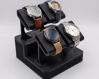 May include: A black watch display stand holding four watches. The watches have various band colors, including brown, blue, and silver. The stand is made of black material and has a tiered design.