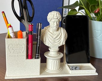 May include: A white desk organizer with a bust of a Roman emperor, a phone holder, and slots for pens and pencils. The organizer has a quote from Marcus Aurelius: "The happiness of your life depends upon the quality of your thoughts."