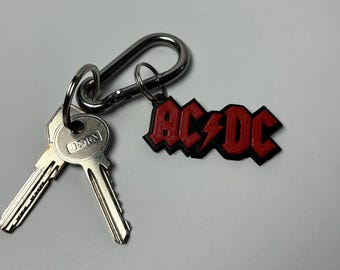 May include: A silver key chain with two keys and a red 3D printed AC/DC logo charm.