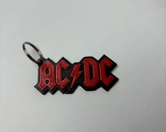 May include: A red and black metal keychain with the word "AC/DC" in bold letters. The keychain has a silver ring for attaching to keys.