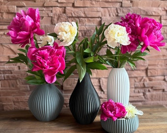 May include: Three vases with a variety of pink and white peonies. The vases are all different shapes and sizes, and they are made of a textured ceramic material. The vases are arranged on a wooden table.
