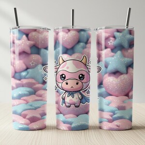 Peut inclure: Trois gobelets en acier inoxydable avec pailles. Les gobelets présentent un motif de cœurs et d'étoiles roses, bleus et blancs. Un gobelet a un dessin de vache de dessin animé avec une cape. Les gobelets sont sur une surface en bois clair.
