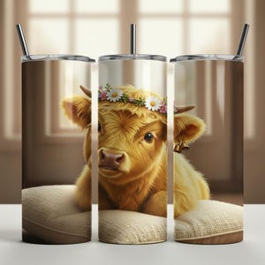 May include: A stainless steel tumbler featuring a digital illustration of a fluffy, golden-brown Highland cow wearing a flower crown and small bells. The cow is resting on a beige pillow. The tumbler has a silver lid and straw.