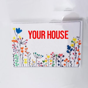 Puede incluir: Un cartel blanco con las palabras "YOUR HOUSE" en letras rojas. El cartel está decorado con un borde de flores de colores hecho con pintura de dedos.