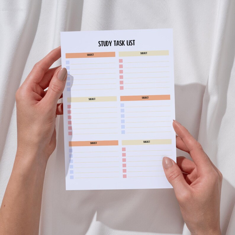May include: A white study task list with the title "STUDY TASK LIST" at the top. The list is divided into sections with the word "SUBJECT" and check boxes in orange, yellow, and blue. The list is held by two hands.