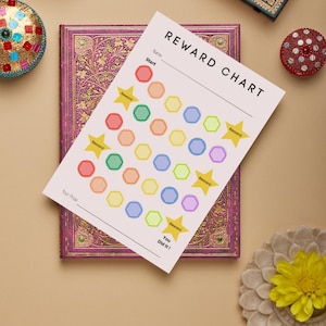 May include: A reward chart with the title "REWARD CHART" and the words "Name", "Start", "Reward", and "Your Prize". The chart has colorful hexagonal shapes and star-shaped reward indicators. The chart is on a purple journal.