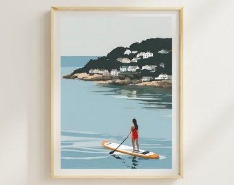 May include: A woman in a red swimsuit stands on a paddleboard in the water. The paddleboard is orange and white. In the background, a green hill with white houses is visible. The sky is blue and the water is a light blue.