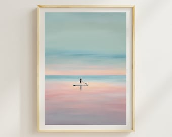 Könnte beinhalten: Ein gerahmtes Gemälde, das eine Person beim Paddelboarden auf einem ruhigen Gewässer bei Sonnenuntergang zeigt. Der Himmel ist in sanftem Blau und Rosa gehalten, und das Wasser spiegelt die Farben des Himmels wider. Das Gemälde ist in einem hellen Holzrahmen gefasst.