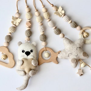 Könnte beinhalten: Ein beige-braunes Baby-Mobile mit einer Wolke, einem Fisch, einem Stern und einem Otter, der einen Stern hält. Das Mobile hat Holzperlen und gehäkelte Perlen.