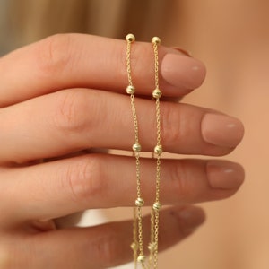 May include: A gold chain necklace with small, round beads. The chain is delicate and has a simple design.