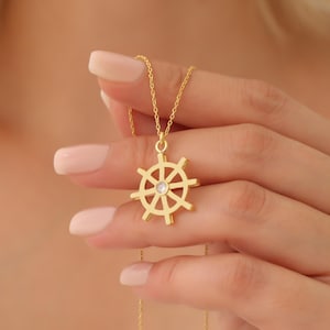 May include: A gold necklace with a small, sparkling, clear stone in the center of a ship's wheel pendant.