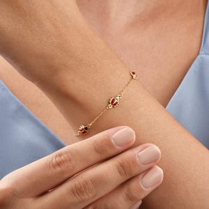 Peut inclure: Un bracelet en or délicat orné de trois breloques coccinelles avec des détails en émail rouge et noir. Le bracelet est porté au poignet, mettant en valeur sa fine chaîne et le design détaillé des pendentifs coccinelles. C'est un bijou.