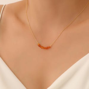 May include: A delicate gold chain necklace with a curved row of small, orange amber beads.