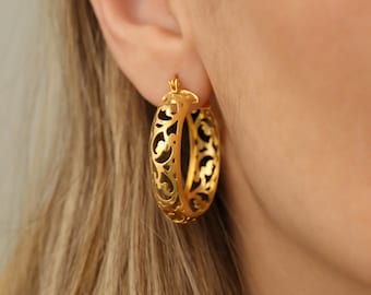 May include: Gold hoop earrings with a delicate, intricate floral design. The earrings are lightweight and have a polished finish.