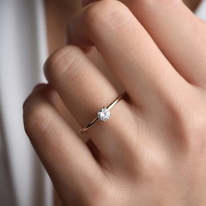 May include: A simple gold band ring with a single round diamond in the center.