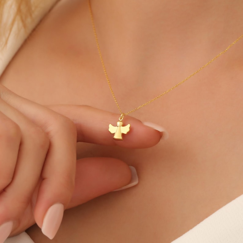 May include: A gold angel pendant necklace. The pendant is a simple, stylized design of an angel with wings.
