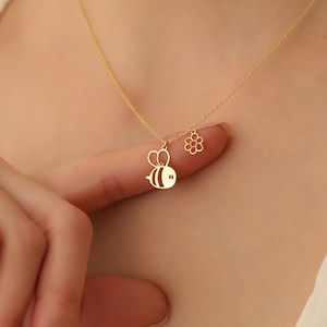 May include: A gold necklace with a bee and flower charm. The bee charm is detailed with black stripes and the flower charm is a simple outline.