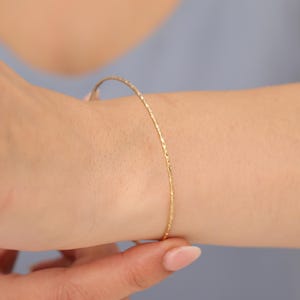 May include: A delicate gold bangle bracelet with a textured finish.