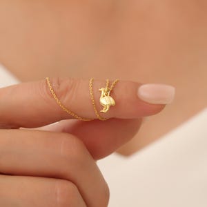 May include: A gold chain necklace with a small gold pendant shaped like a bird.