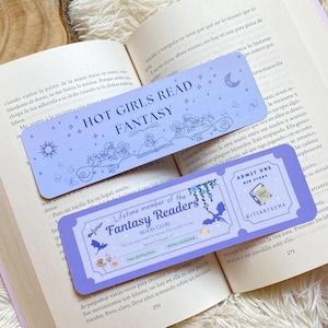 Könnte beinhalten: Zwei Lesezeichen liegen auf einem offenen Buch. Das obere Lesezeichen lautet "HOT GIRLS READ FANTASY" mit floralen und himmlischen Designs. Das untere Lesezeichen ist ein Ticket für den "Fantasy Readers BOOK CLUB".