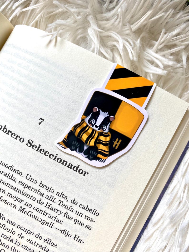 May include: A yellow and black striped bookmark with a cartoon badger wearing a yellow and black scarf. The bookmark has a large "H" on it.