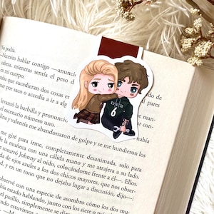 Puede incluir: Un marcapáginas con una pareja de dibujos animados abrazándose, con el texto "LYNCH 6" en la camisa del chico. El marcapáginas está en un libro abierto con texto impreso.