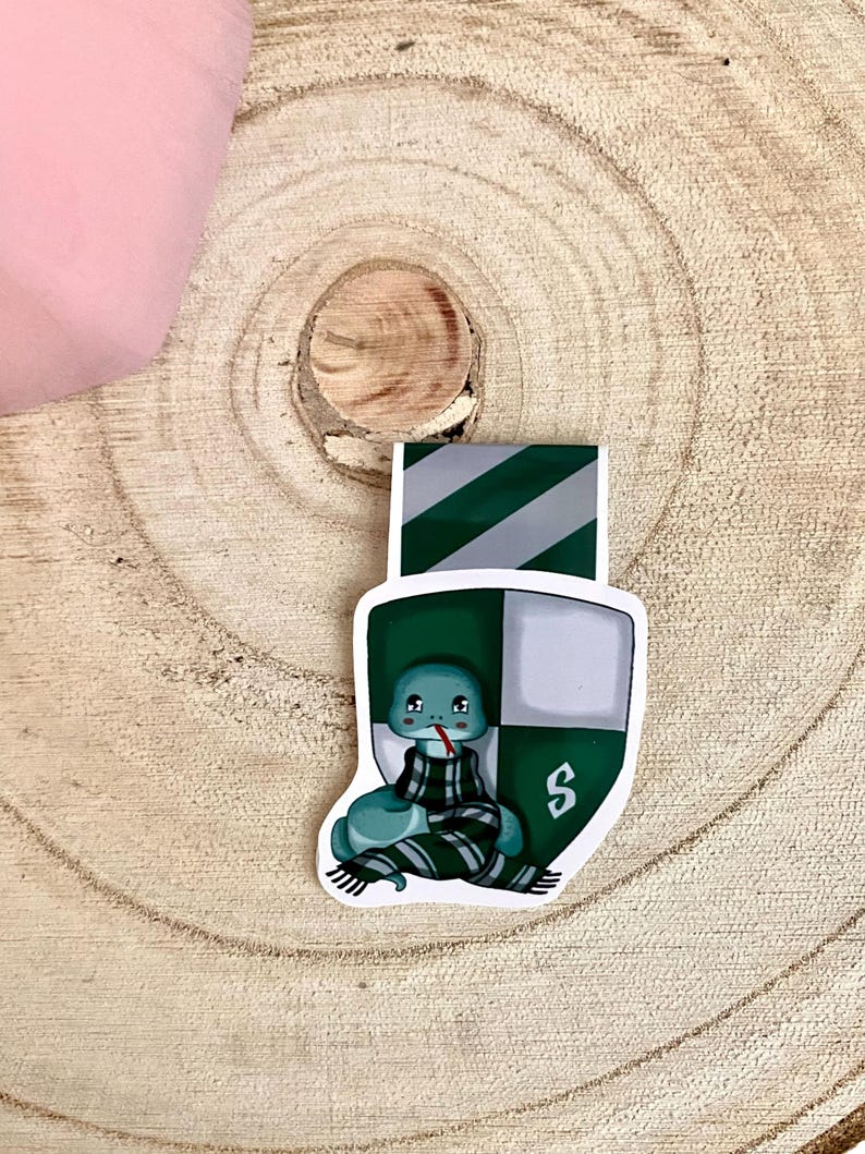 May include: A green and white bookmark with a cartoon snake wearing a green and white scarf. The bookmark has the letter "S" on it.